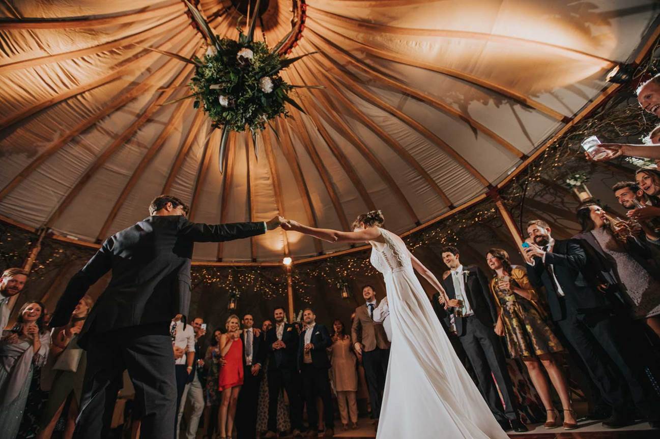 Bride and groom first dance in tent with friends and family surrounding